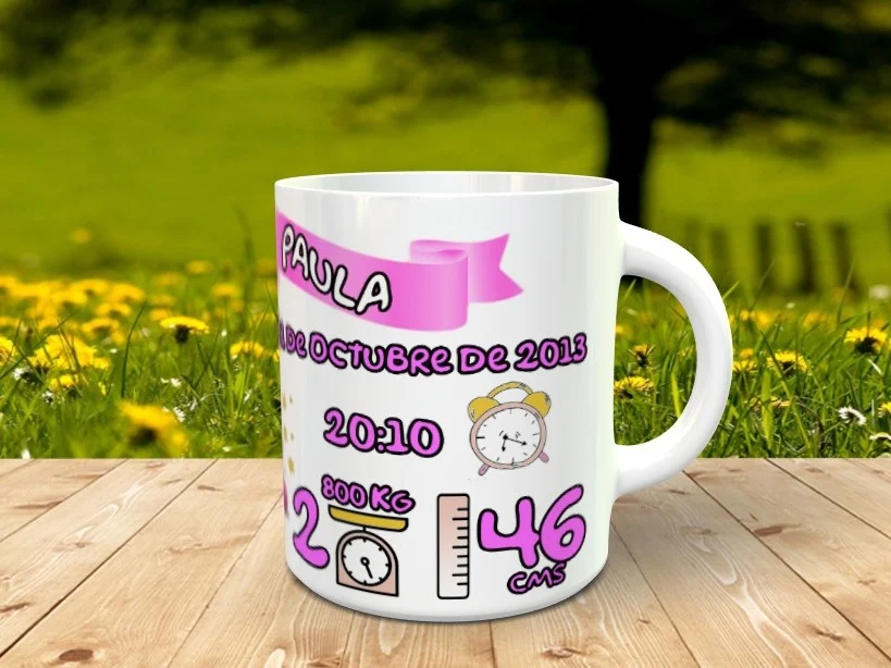 Taza blanca personalizable con datos de nacimiento de bebé en tonos rosados y morados, apoyada sobre listones de madera ante un fondo campestre desenfocado.