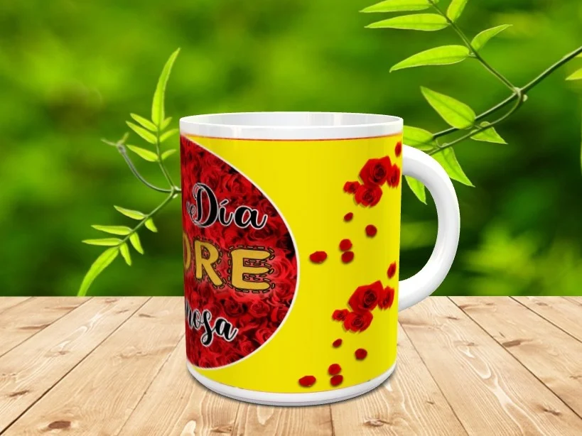 Taza blanca de cerámica personalizada para el Día de la Madre con fondo amarillo, un círculo de rosas rojas y texto visible. La pieza descansa sobre una superficie de madera con vegetación difusa de fondo.