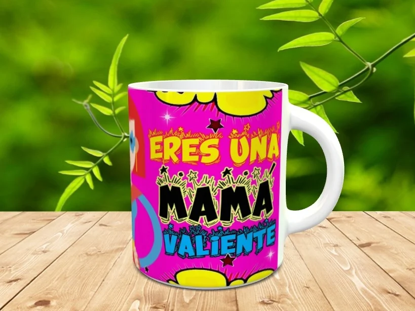 Taza blanca de cerámica personalizada con diseño estilo cómic en tonos fucsia y amarillo con el texto Eres una mamá valiente, apoyada sobre una superficie de madera.
