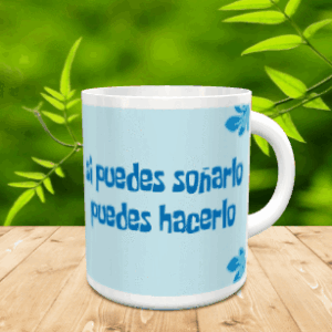 Taza de cerámica blanca con frase motivacional en azul sobre fondo celeste y detalles florales, apoyada sobre una superficie de madera.