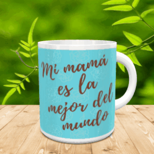 Taza de cerámica blanca con fondo azul claro y la frase Mi mamá es la mejor del mundo, sobre una superficie de madera.