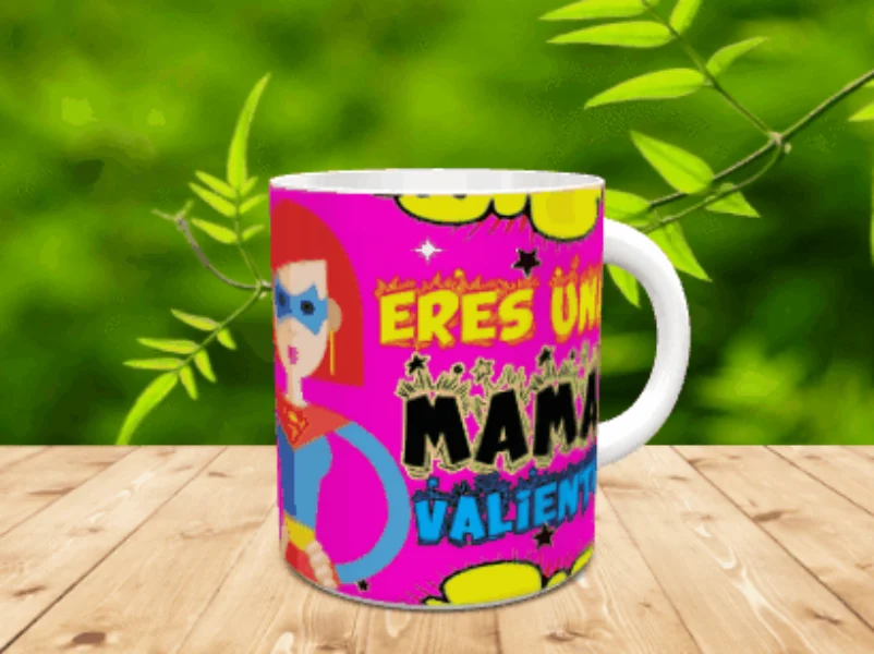 Taza de cerámica blanca con diseño de superheroína y el texto Eres una mamá valiente, apoyada sobre una superficie de madera.