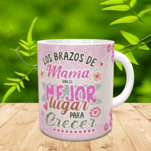 Taza de cerámica blanca con asa, decorada con un diseño en tonos rosas y texto emotivo dedicado a las madres. La pieza reposa sobre una superficie de madera con vegetación de fondo.