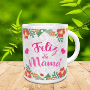 Taza blanca de cerámica personalizada con el texto Feliz día Mamá en tonos rosas, rodeada de detalles florales y corazones, colocada sobre una superficie de madera con fondo verde difuminado.