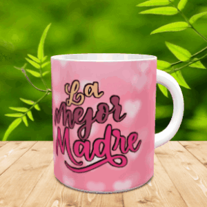 Taza blanca de cerámica personalizada con el texto La Mejor Madre sobre fondo rosa con corazones, dispuesta sobre una superficie de madera.
