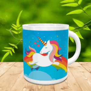 Taza de cerámica blanca con un diseño infantil de unicornio sobre un arco iris y fondo azul de nubes y estrellas. La pieza se sitúa sobre una superficie de madera.