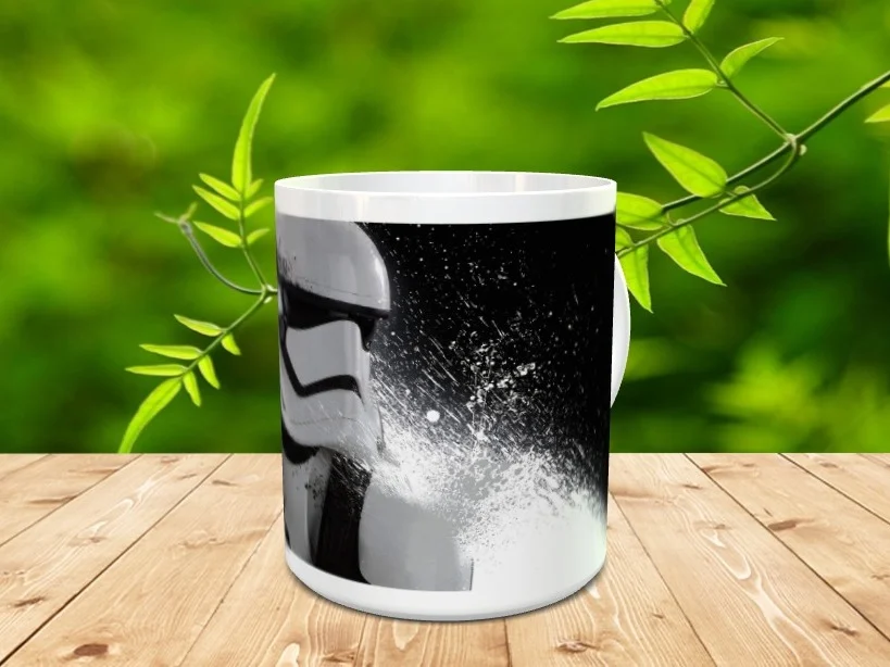Taza de cerámica blanca decorada con la ilustración monocromática de un soldado imperial sobre un fondo oscuro salpicado. La pieza descansa sobre una superficie de madera con vegetación desenfocada.