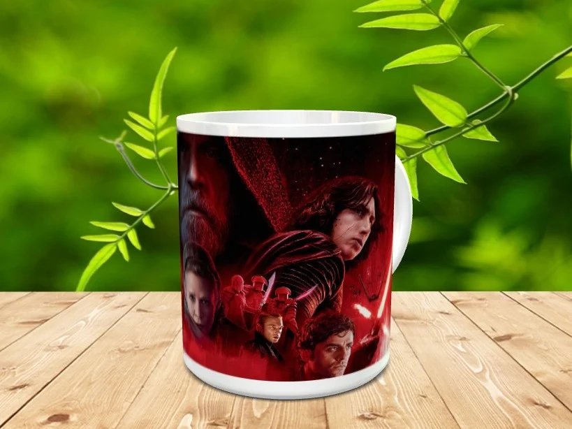Taza de cerámica blanca decorada con una composición de varios personajes en tonos rojizos, sobre superficie de madera con vegetación al fondo.