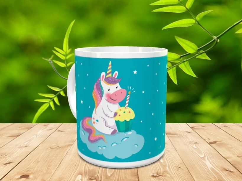 Taza de cerámica blanca con diseño de un unicornio sobre una nube con una magdalena de cumpleaños y fondo azul con estrellas.