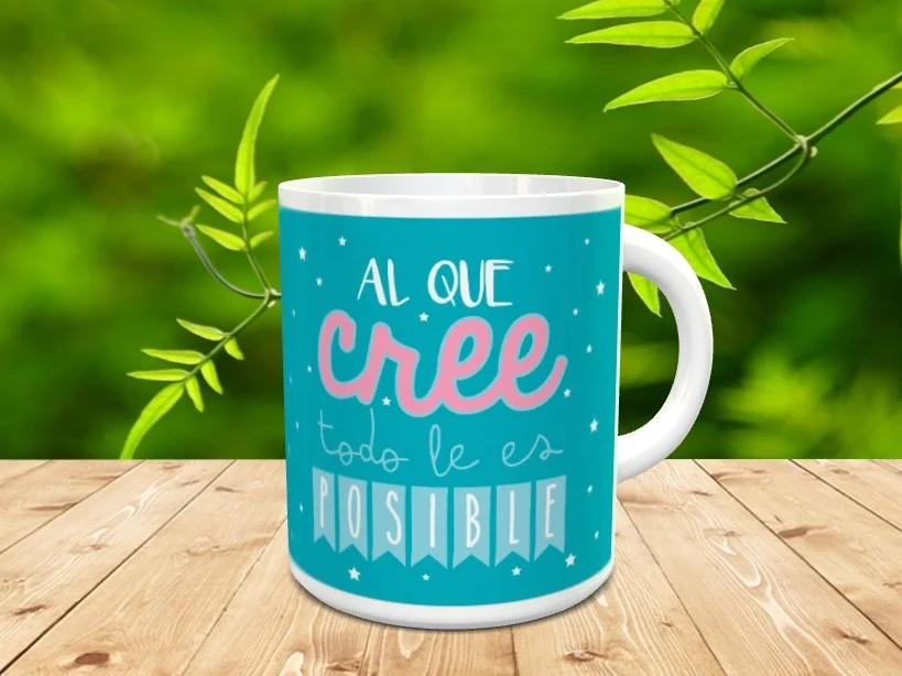 Taza de cerámica blanca con fondo azul y el mensaje Al que cree todo le es posible sobre superficie de madera.
