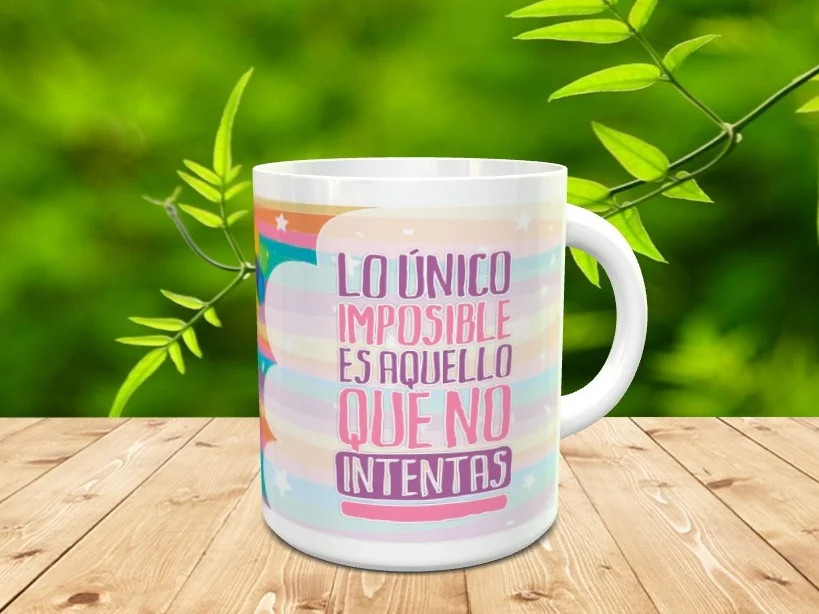 Taza de cerámica blanca con frase motivacional y diseño de arcoíris sobre fondo pastel, apoyada en madera.