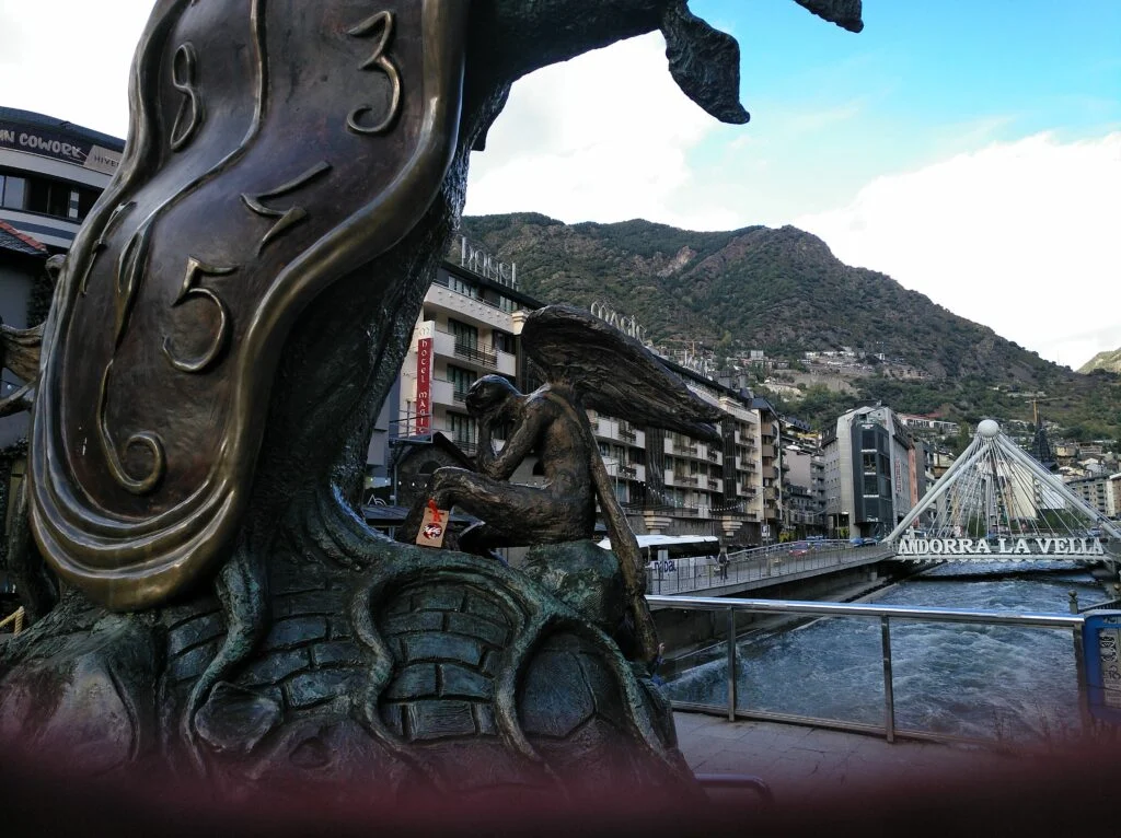 Fotografía exterior de la escultura de bronce La Noblesa del Temps en Andorra la Vella, con un reloj blando y un ángel sentado.