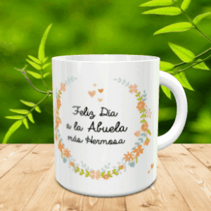 Taza blanca de cerámica decorada con una corona de flores y la frase Feliz Día a la Abuela más Hermosa, apoyada sobre listones de madera.