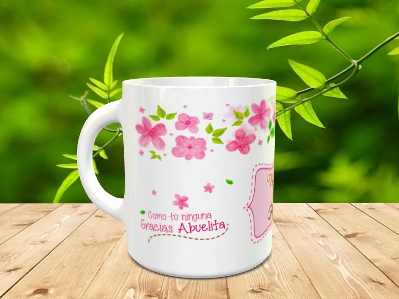 Taza blanca de cerámica personalizada con flores rosas y la frase Como tú ninguna Gracias Abuelita sobre superficie de madera y fondo natural.