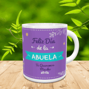 Taza de cerámica blanca con fondo morado y detalles turquesas con el texto Feliz Día de la Abuela sobre una mesa de madera.
