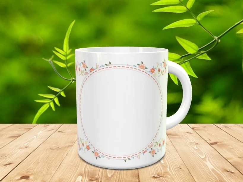 Taza blanca de cerámica con un marco circular pespunteado y cenefas florales, sobre una superficie de madera con fondo natural desenfocado.