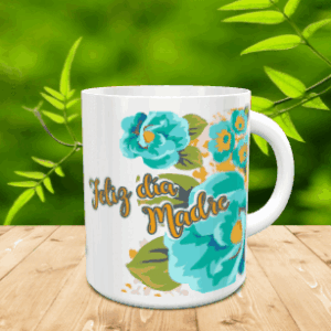 Taza blanca de cerámica en movimiento con un diseño de flores turquesas y el mensaje Feliz día Madre, situada sobre una superficie de madera con fondo verde difuminado.