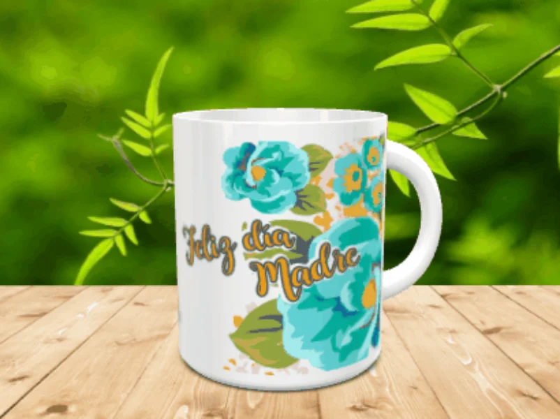 Taza blanca de cerámica en movimiento con un diseño de flores turquesas y el mensaje Feliz día Madre, situada sobre una superficie de madera con fondo verde difuminado.