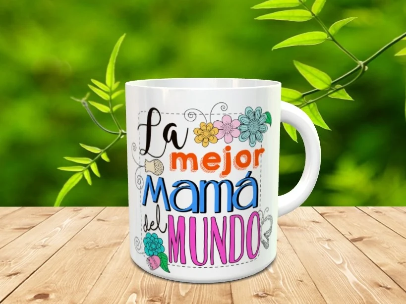 Taza blanca de cerámica decorada con la frase La mejor Mamá del Mundo junto a motivos florales y mariposas, situada sobre una superficie de madera.