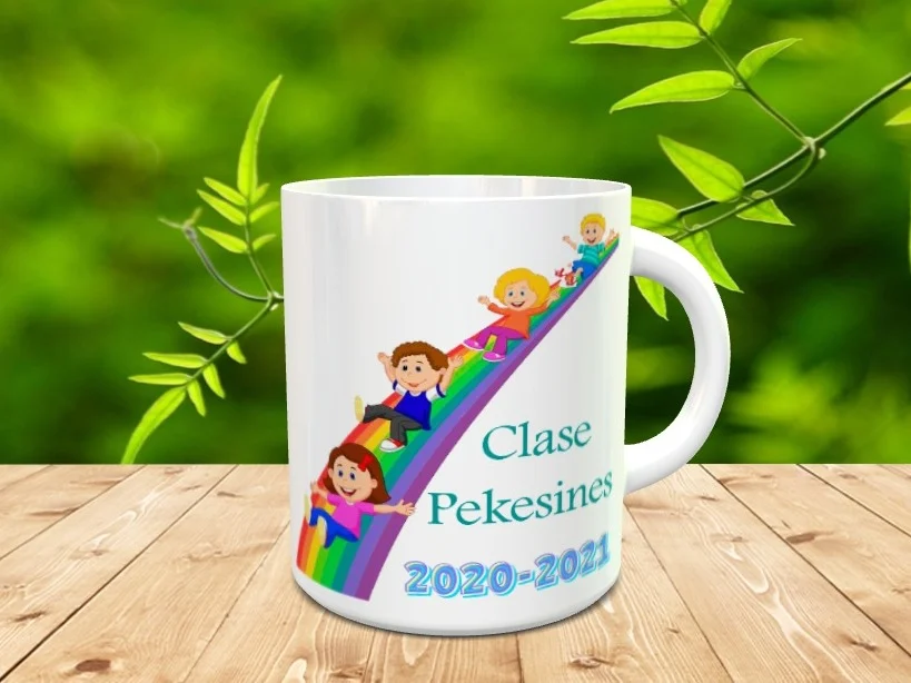 taza blanca de cerámica con un diseño infantil en el que varios niños se deslizan por un arcoíris junto al texto Clase Pekesines 2020-2021. Ref. 8xx