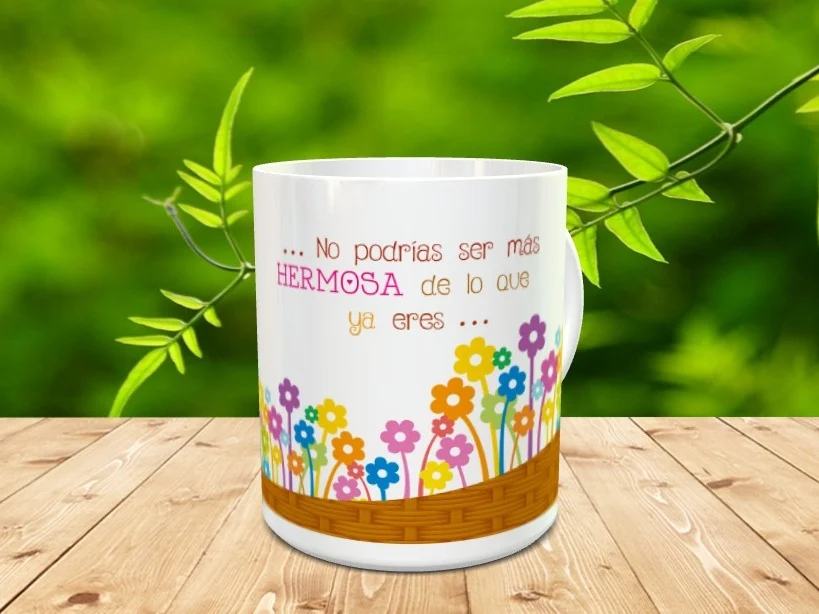 Taza blanca de cerámica decorada con un cesto inferior de flores y la frase No podrías ser más hermosa de lo que ya eres, sobre superficie de madera.