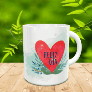 Taza blanca de cerámica en movimiento decorada con un gran corazón rojo y la frase Feliz Día sobre fondo acuarelado y ramas verdes, situada sobre una superficie de madera.