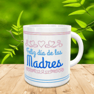 Taza blanca de cerámica decorada con el mensaje Feliz día de las Madres en azul y detalles en rosa sobre una mesa de madera con fondo vegetal.