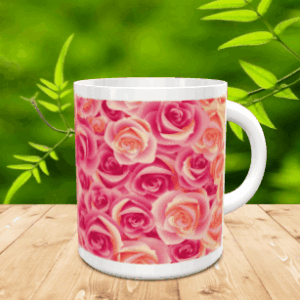 Taza blanca de cerámica decorada con un diseño integral de rosas en tonos rosados y anaranjados, situada sobre una superficie de madera frente a un fondo vegetal desenfocado.