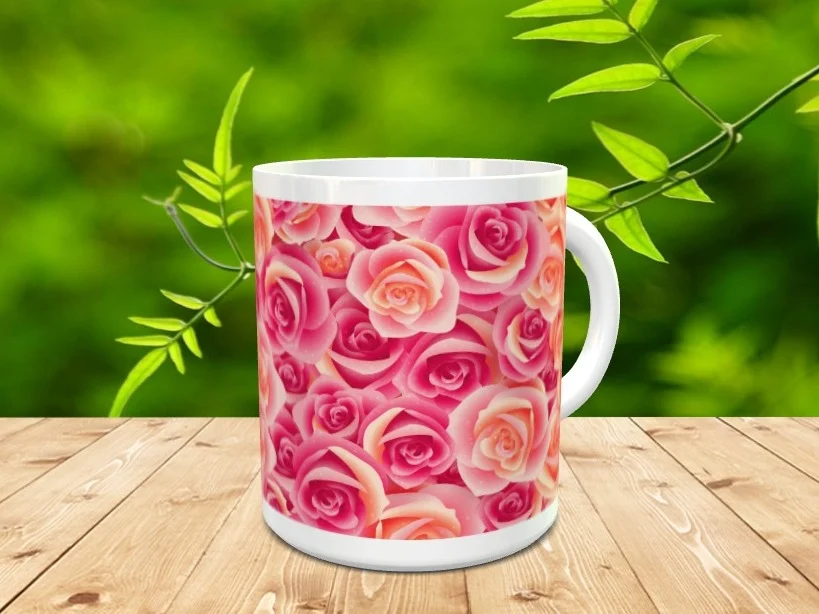 Taza blanca de cerámica decorada con un estampado de rosas en tonos rosas y anaranjados sobre una superficie de madera y fondo natural difuminado.