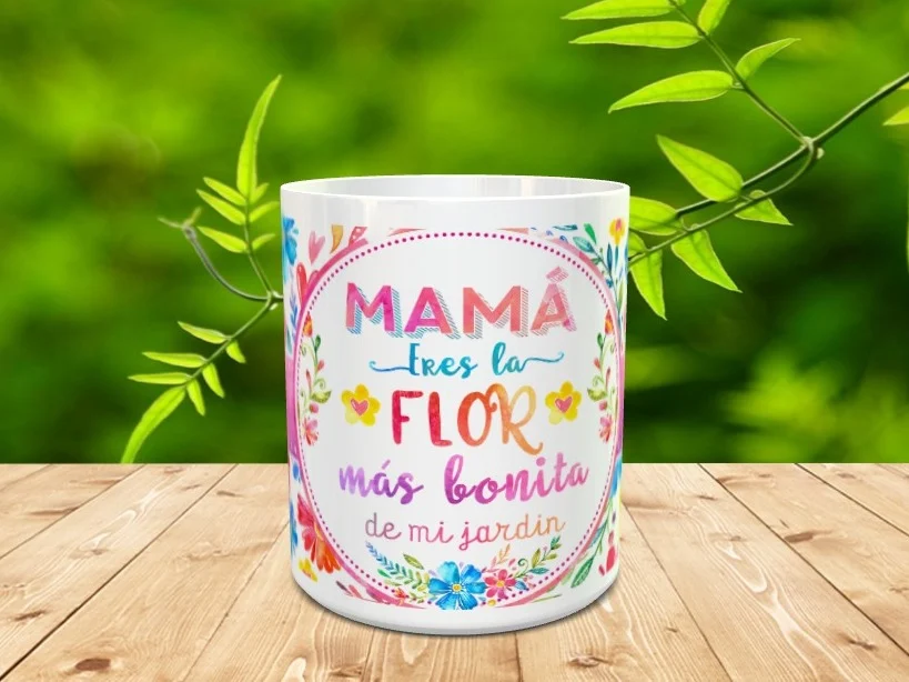 Maqueta de taza blanca de cerámica con un diseño floral y la frase Mamá eres la flor más bonita de mi jardín sobre una superficie de madera.