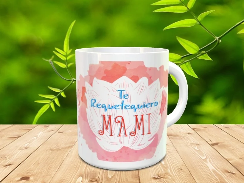 Taza blanca de cerámica decorada con una flor de loto sobre fondo acuarela rosa y la frase Te Requetequiero Mami, colocada sobre madera con fondo natural.