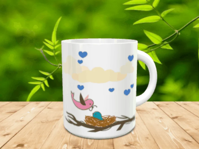 Taza blanca de cerámica con diseño de nido de pájaros, nubes y corazones azules sobre superficie de madera.