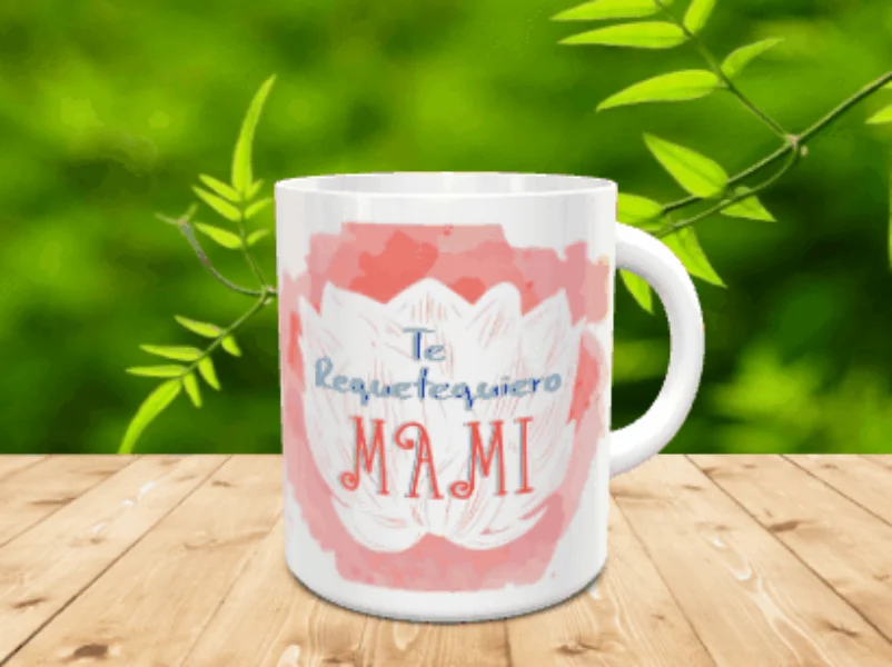 Taza blanca de cerámica con diseño de flor de loto sobre mancha rosa y texto Te Requetequiero Mami, apoyada sobre listones de madera.