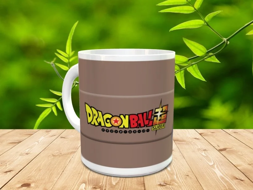 Taza blanca de cerámica decorada con el logotipo de Dragon Ball Super sobre fondo marrón. Se sitúa en una mesa de madera con vegetación difuminada al fondo.