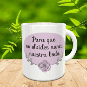 Maqueta de taza blanca de cerámica con un óvalo lila, la frase Para que no olvides nunca nuestra boda y un detalle floral sobre una mesa de madera.