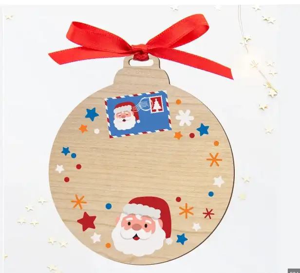 Adorno redondo de Navidad fabricado en madera natural, rematado con un lazo rojo. Los bordes están decorados con simpáticas ilustraciones infantiles de Papá Noel, un sello postal y estrellitas, dejando un amplio espacio central vacío para personalizar con un nombre.