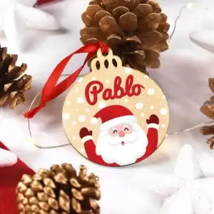 Fotografía decorativa de un adorno navideño blanco personalizado con el nombre Pablo y una ilustración de Papá Noel. El adorno destaca sobre un fondo festivo acompañado de piñas secas de pino, estrellas blancas y luces cálidas.